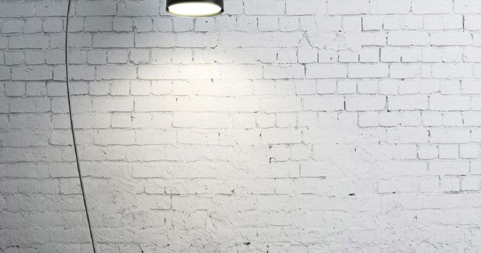 Zu sehen ist eine schwarze Stehlampe vor einer weißen Bruchsteinmauer.