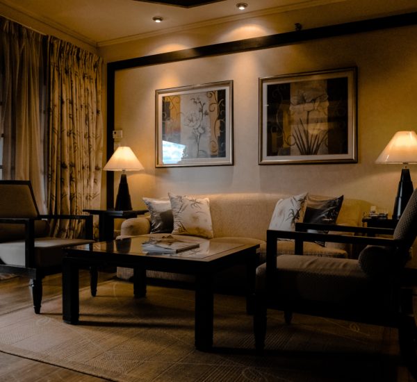 Zu sehen ist ein Wohnbereich mit 2 Tischlampen, einer Coach, 2 Sesseln und einem kleinen quadratförmigenTisch